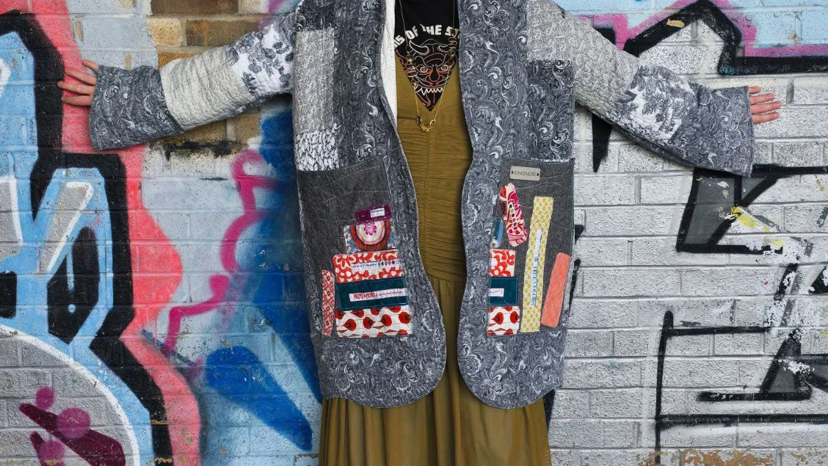 A patchwork quilted vest with appliquéd pockets, worn with arms outstretched against a graffiti wall